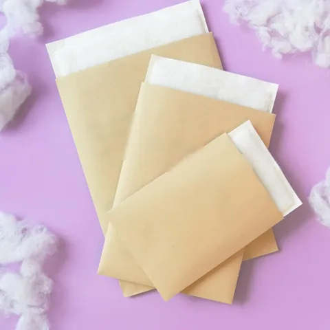 Trois enveloppes matelassées en papier kraft, de tailles différentes, sur un fond mauve